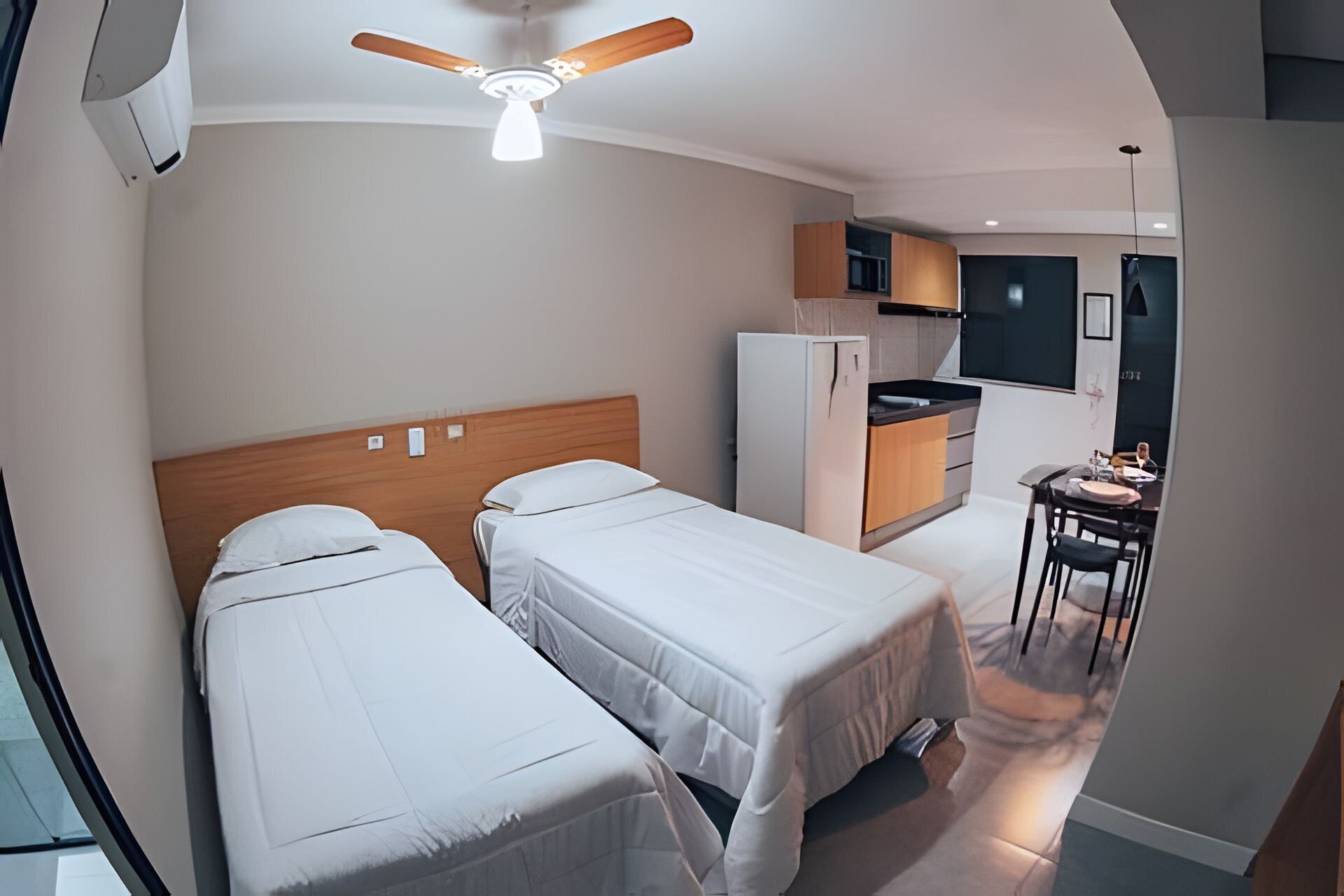 A compact hotel room with two single beds, a kitchenette, a ceiling fan, and a dining area.