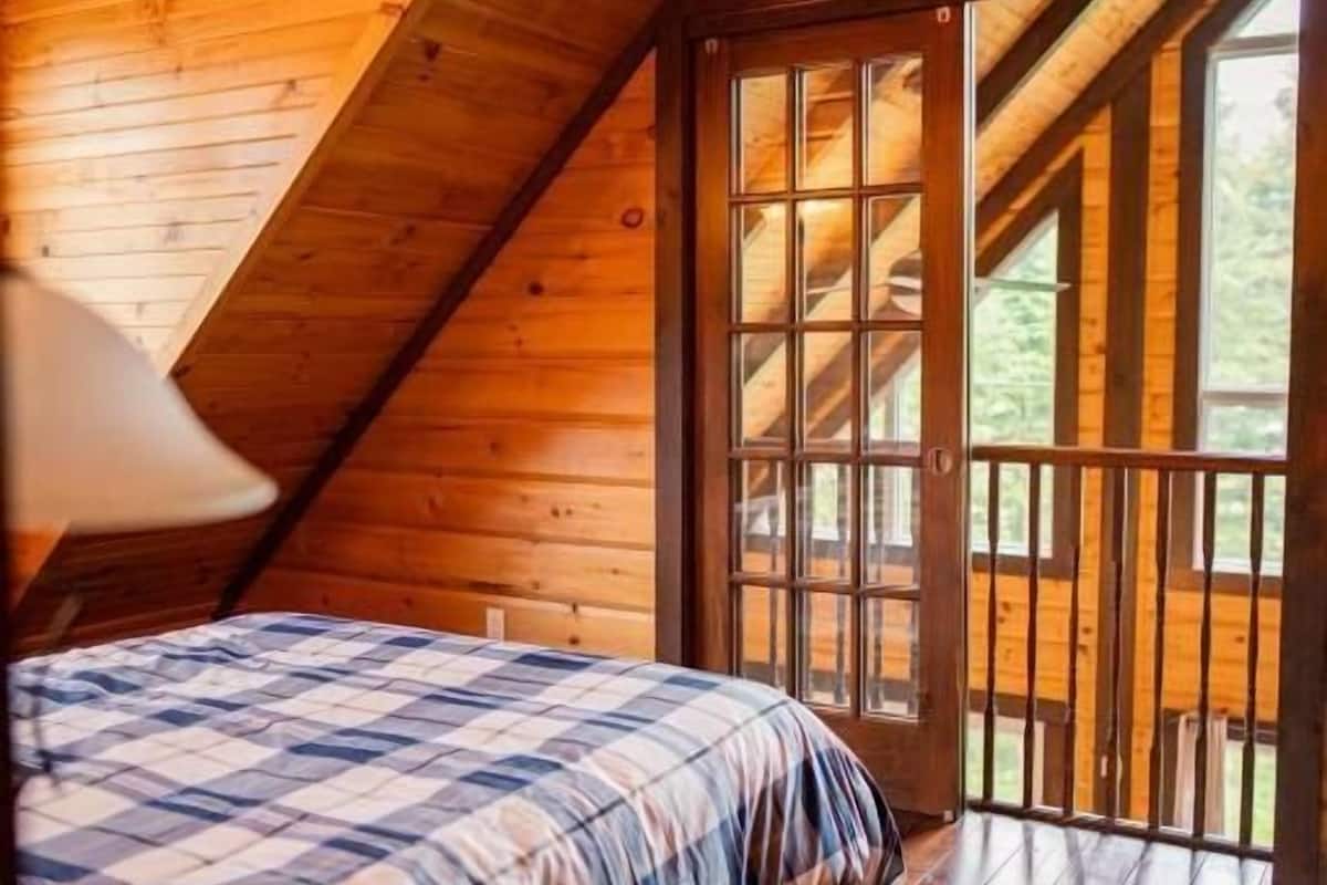Un dormitorio tipo cabaña de madera con una cama, una mesita de noche y una ventana.