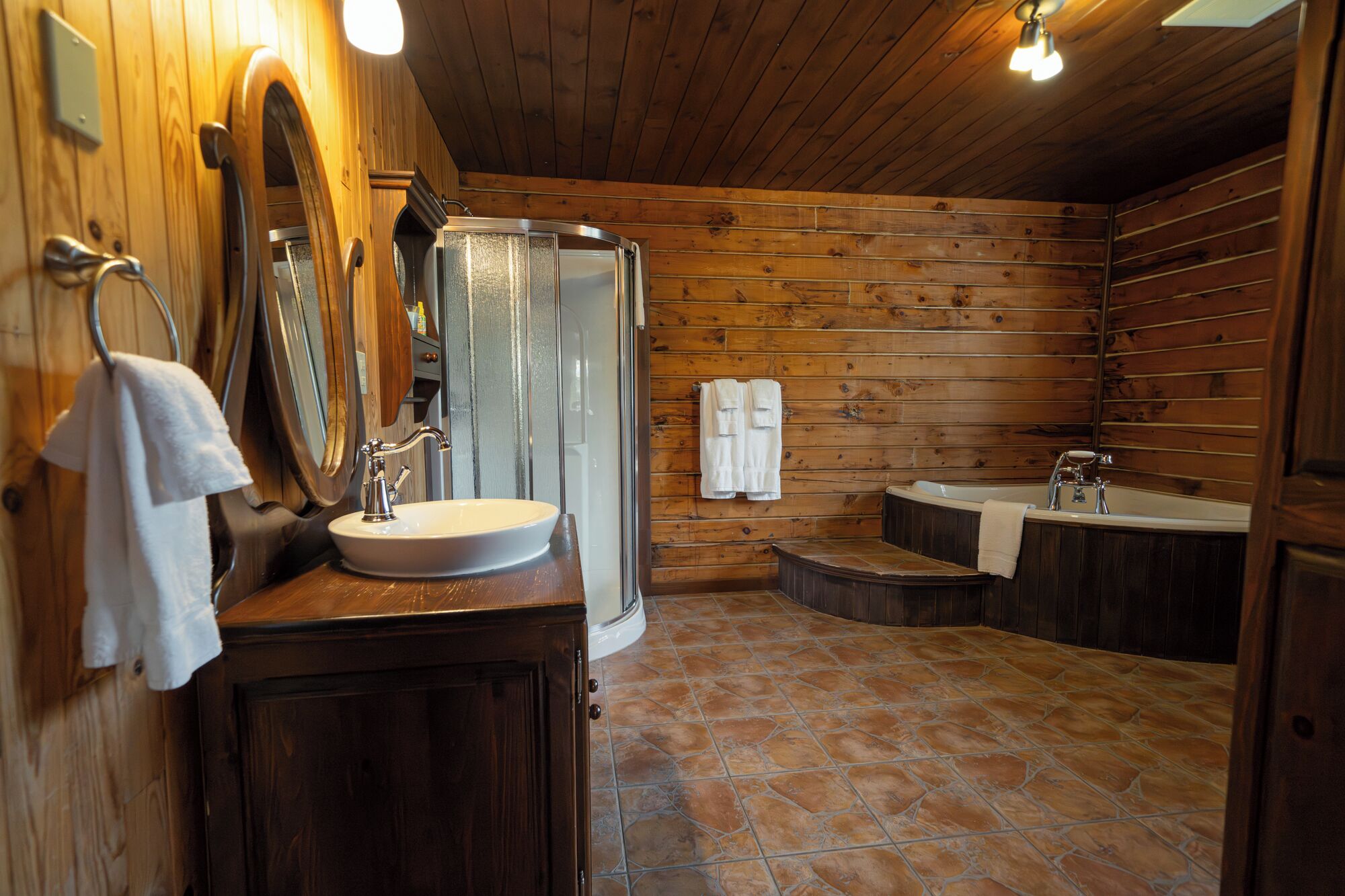 Een houten badkamer met een badkuip, douche, wastafel en spiegel.