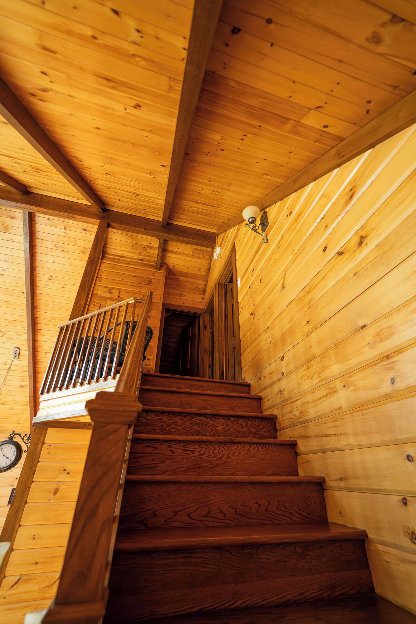 Eine Holztreppe führt zu einer zweiten Etage, mit Handlauf und einer Wandleuchte.