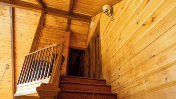 Eine Holztreppe führt zu einer zweiten Etage, mit Handlauf und einer Wandleuchte.