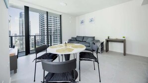 A modern living room with a round dining table, grey sofa, and a view of tall buildings. - 34th Floor Luxurious 1BR - Epic View & Top Location (Miami)