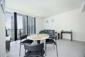Ein modernes Wohnzimmer mit einem runden Esstisch, einem grauen Sofa und Blick auf hohe Gebäude.