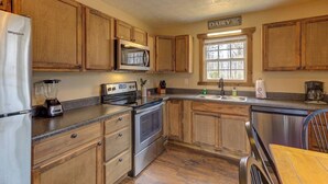 Una cocina con armarios de madera, refrigerador, microondas, horno, lavavajillas y ventana con vistas.
