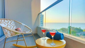 Un balcón con una mecedora de mimbre, una pequeña mesa redonda con dos copas de vino tinto y vista al mar.