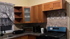 A kitchen with wooden cabinets, a microwave, a stove, and a tiled backsplash. - Terrific 2-bedroom house with AC in Montego Bay (Montego Bay)