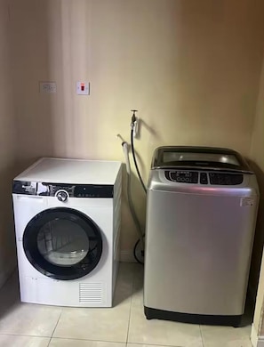 A compact laundry room with a front-loading washer and a top-loading dryer. - Terrific 2-bedroom house with AC in Montego Bay (Montego Bay)