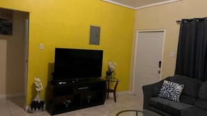A living room with a flat-screen TV, a sofa, a glass coffee table, and a door. - Terrific 2-bedroom house with AC in Montego Bay (Montego Bay)