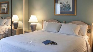 Un lit bien fait, avec un livre bleu posé dessus, un tableau encadré accroché au mur et un miroir qui reflète une partie de la pièce.