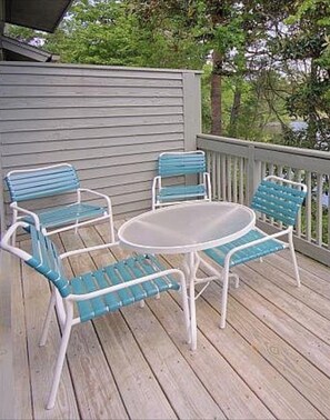 A deck with a round table and four chairs, surrounded by a wooden deck and a railing.