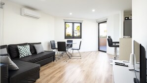 A modern living room with a black sofa, a dining table with chairs, a TV, and an air conditioning unit. - Vilamoura Secret - City center with pool by HD (Vilamoura)