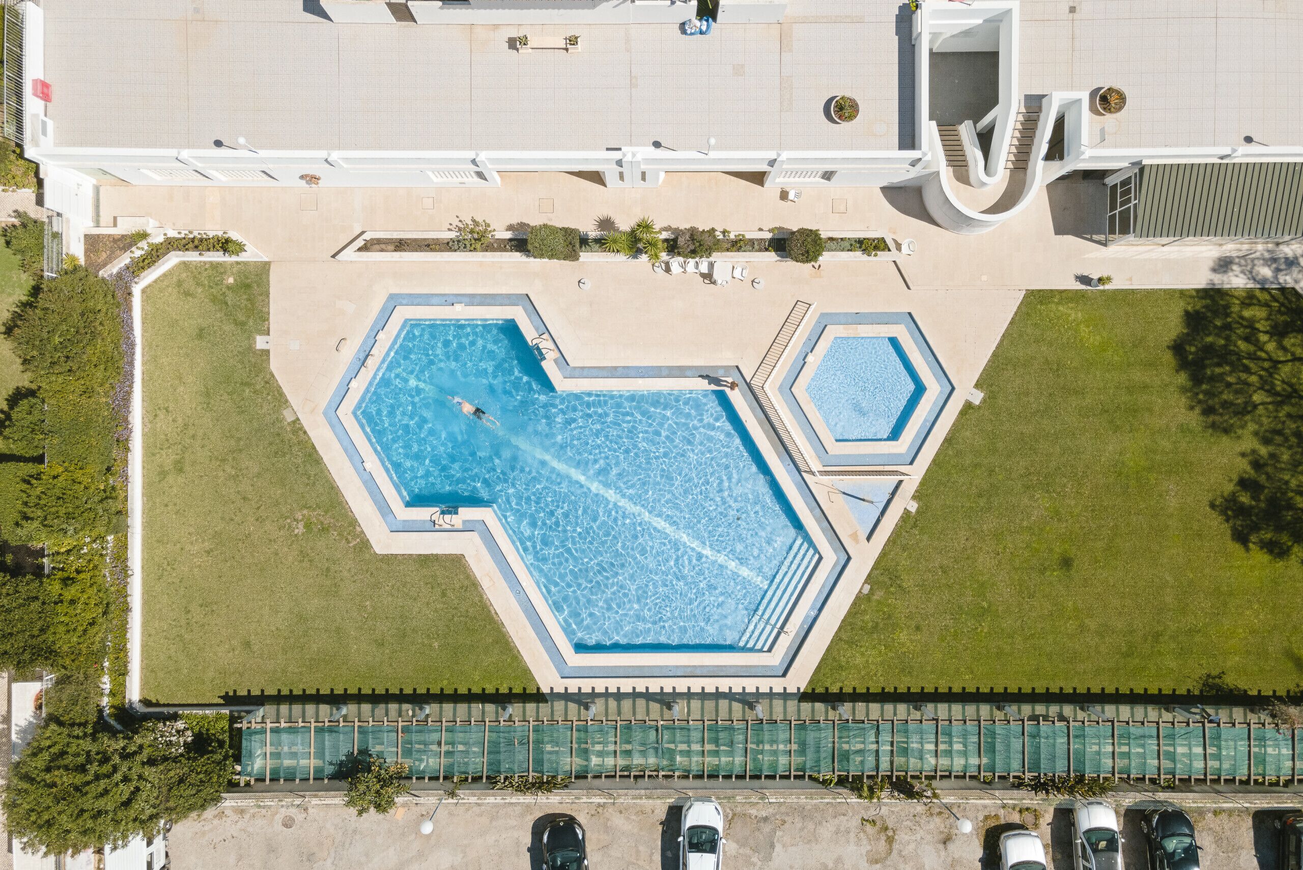 An aerial view of a hotel with a large swimming pool, a covered outdoor area, and a parking lot.
