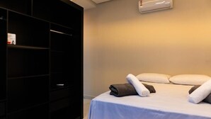 A hotel room with a bed, pillows, a wardrobe, and an air conditioning unit. - Condomínio Triangulo da Embauba  (Porto Seguro)