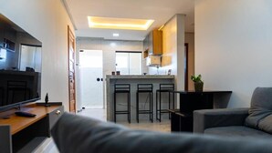 A modern living room with a sofa, a TV, and a kitchen area with a bar stool. - Condomínio Triangulo da Embauba  (Porto Seguro)