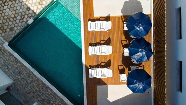 An aerial view of a pool area with a wooden deck, lounge chairs, and umbrellas. - Condomínio Triangulo da Embauba  (Porto Seguro)