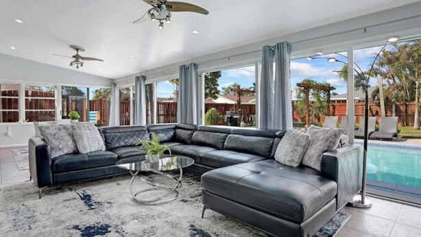A modern living room with a sectional sofa, a coffee table, and a ceiling fan. - 3/2 Heated Pool home Walking Distance to beach (Naples)