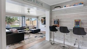 A modern interior with a sofa set, a bar area, and a sign reading 'BEACH HOUSE.' - 3/2 Heated Pool home Walking Distance to beach (Naples)