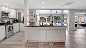 A modern kitchen with white cabinetry, a central island, and a view into a living area. - 3/2 Heated Pool home Walking Distance to beach (Naples)