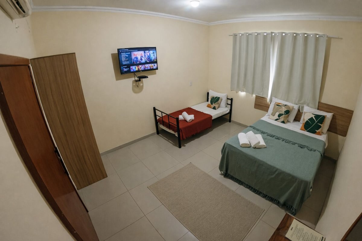 A hotel room with two beds, a TV, a window with curtains, and a wooden door.