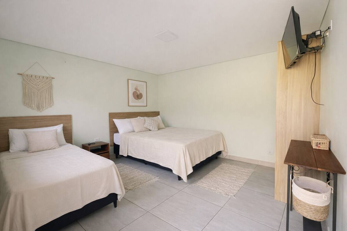 A bedroom with two beds, a bedside table, a wall-mounted TV, and a small wooden shelf with a basket.
