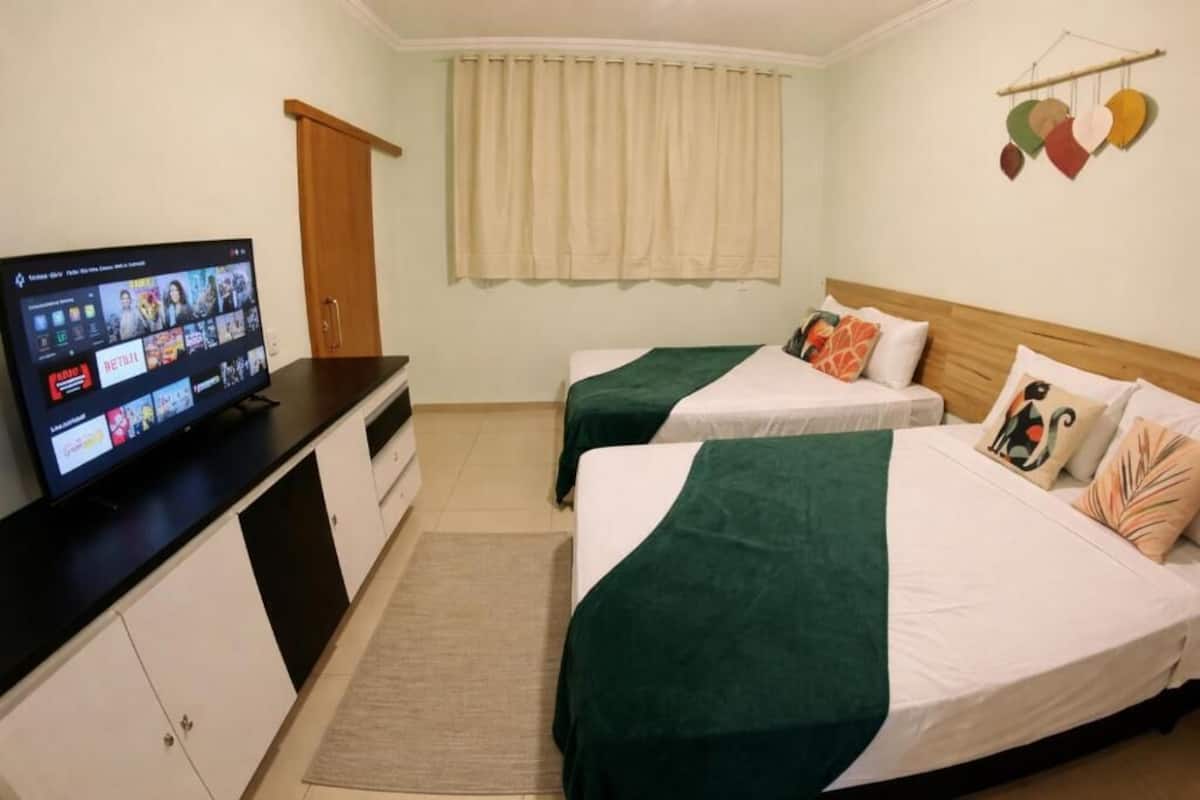 A hotel room with two beds, a TV on a dresser, a window with curtains, and a wall decoration.