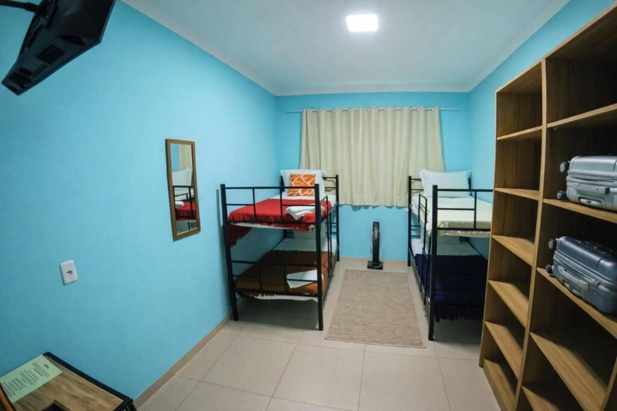 A room with two bunk beds, a mirror, a shelf with luggage, and a window with curtains.