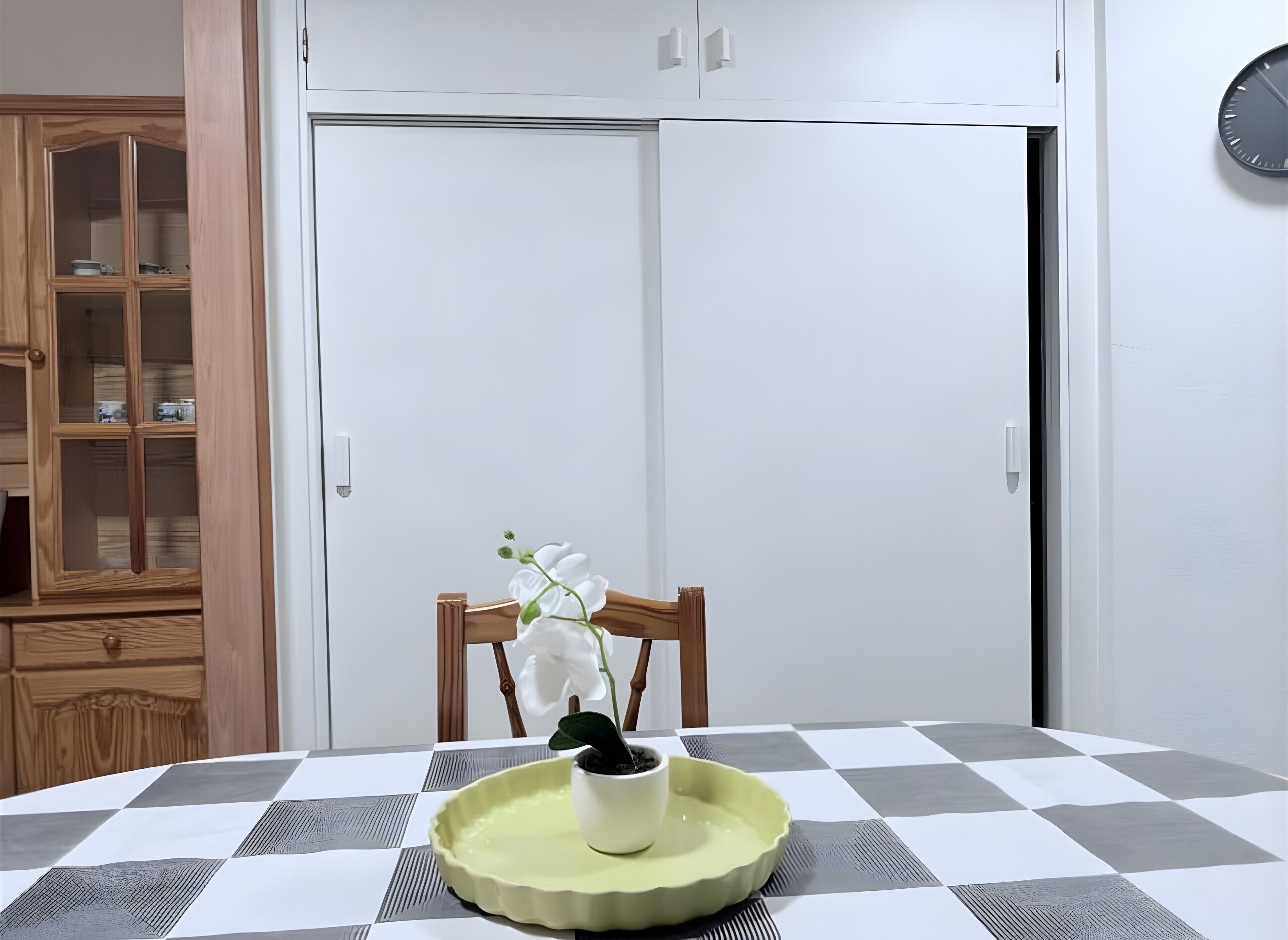 Un comedor con mantel a cuadros, una planta en maceta y un mueble con puertas de cristal.