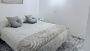 Een minimalistische slaapkamer met een bed, kussens, een nachtkastje en een wandlamp.