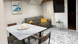 Een moderne woonkamer met een eettafel, een grijze bank en een schilderij aan de muur.