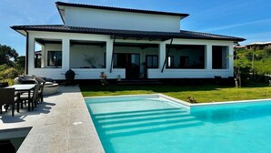 Ett modernt hus med en swimmingpool, utomhusmöbler och en välskött gräsmatta.