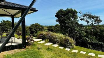 A modern outdoor area with a covered seating area, a grassy lawn, and a pathway leading to a scenic view.