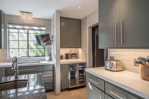 A modern kitchen with grey cabinetry, a built-in oven, a toaster, and a window with a view of greenery. - Spacious 5-bedroom villa •Large Infinity Pool •Spa •Game Room •Striking View (Thousand Palms)