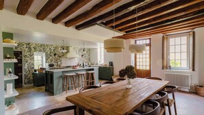 A rustic kitchen with exposed wooden beams, a central island with stools, and a dining table with chairs. - Manoir de charme en Normandie | piscine chauffée à moins de 2h de Paris. (Chambord)