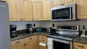 A kitchen with wooden cabinets, a stainless steel microwave, a coffee maker, a mixer, a toaster, and an oven. - Charming 2-bedroom apartment with AC in perfect Naples (Naples)