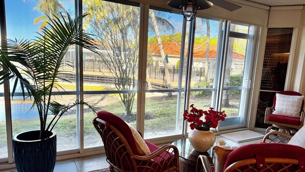 A room with large windows, a ceiling fan, wicker chairs, a potted plant, and a vase with flowers. - Charming 2-bedroom apartment with AC in perfect Naples (Naples)