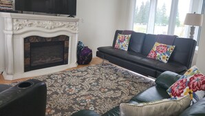 A living room with a fireplace, a flat-screen TV, a sofa with floral cushions, and a patterned rug.