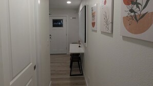 Käytävä, jossa on valkoinen ovi, valkoinen pöytä, jossa on kasvi, ja seinätaidetta.