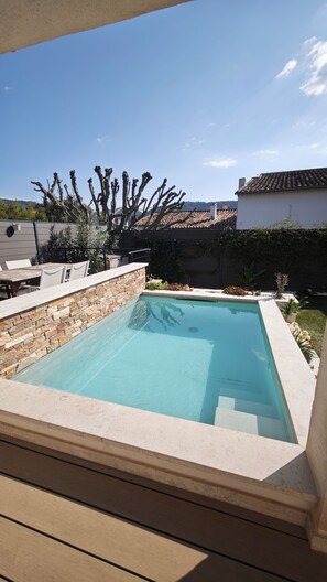 Une piscine rectangulaire bordée de pierres, entourée d’une terrasse aménagée avec du mobilier d’extérieur.