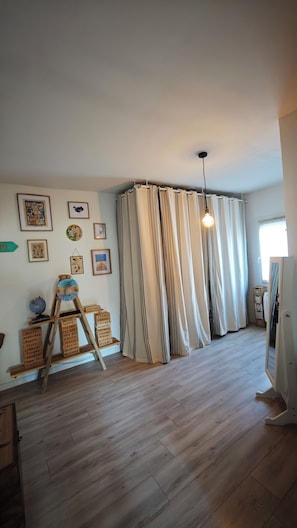 Ein Zimmer mit Holzboden, einem großen Fenster mit Vorhängen und Wandbildern.