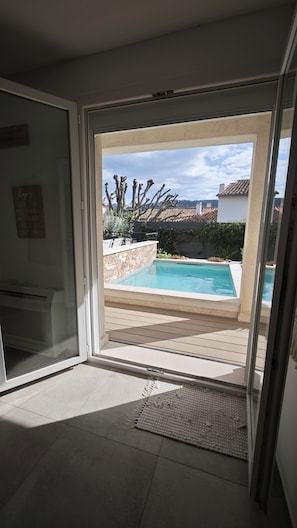 Blick durch eine Glastür auf einen Pool mit einer Steinmauer und einer Pergola.