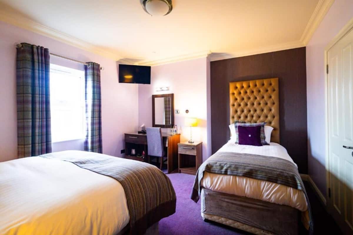 A hotel room with two beds, a desk, a chair, a television, and a window with curtains.