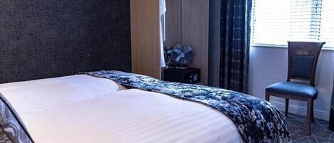 Habitación de hotel con una cama, una silla, perchero y una ventana con persianas.