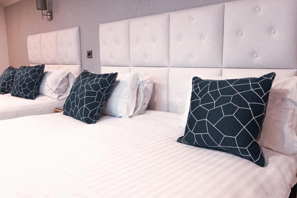 A hotel room with a large bed, a headboard, and a wall-mounted light fixture.