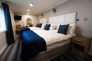 Quarto de hotel com duas camas, uma televisão, um espelho e uma mesinha de cabeceira.