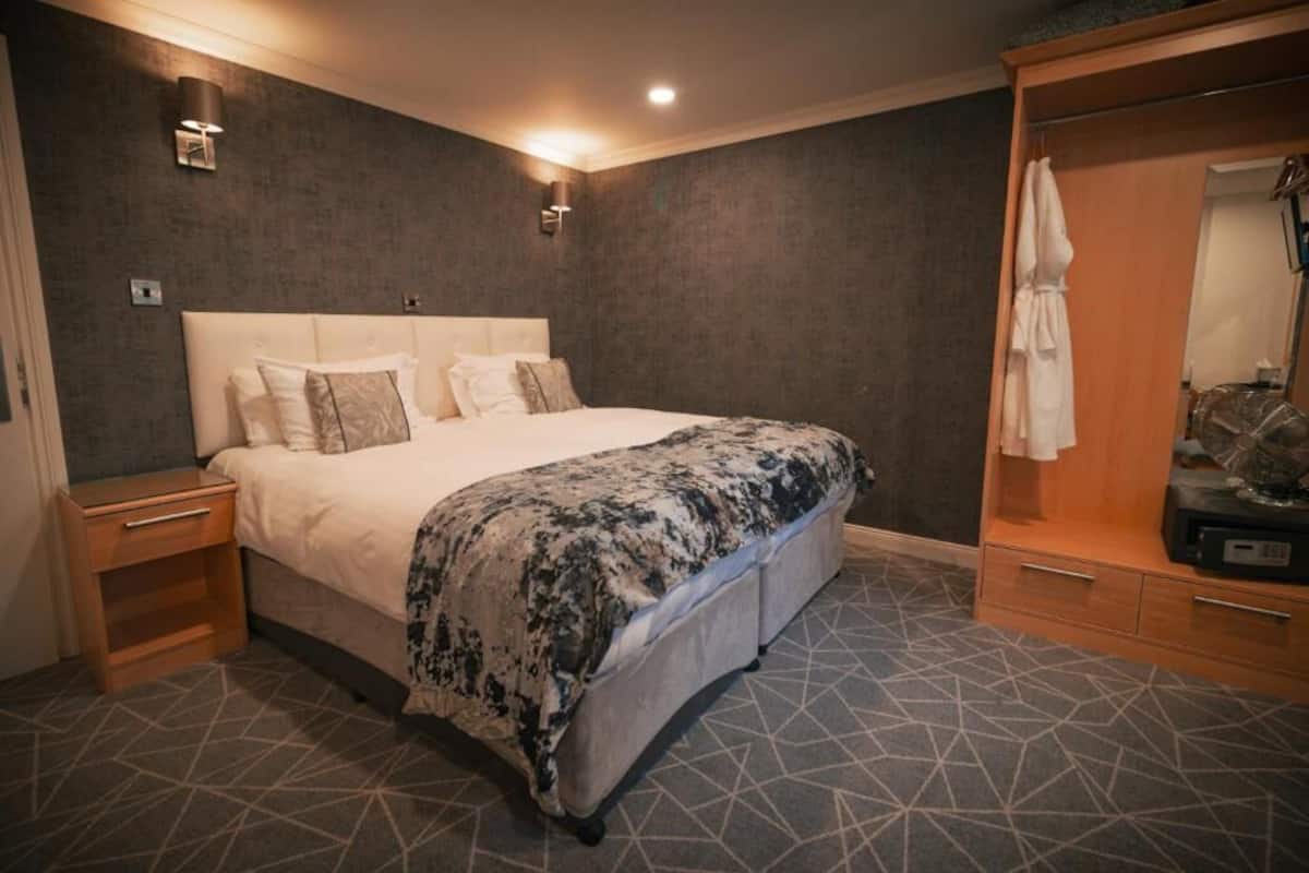 A hotel room with a large bed, a wooden nightstand, a wardrobe, and a mirror.