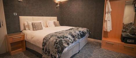 A hotel room with a large bed, a wooden nightstand, a wardrobe, and a mirror.