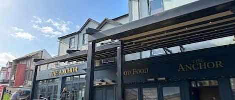A building with 'The Anchor' signage, a covered outdoor seating area, and a visible entrance.