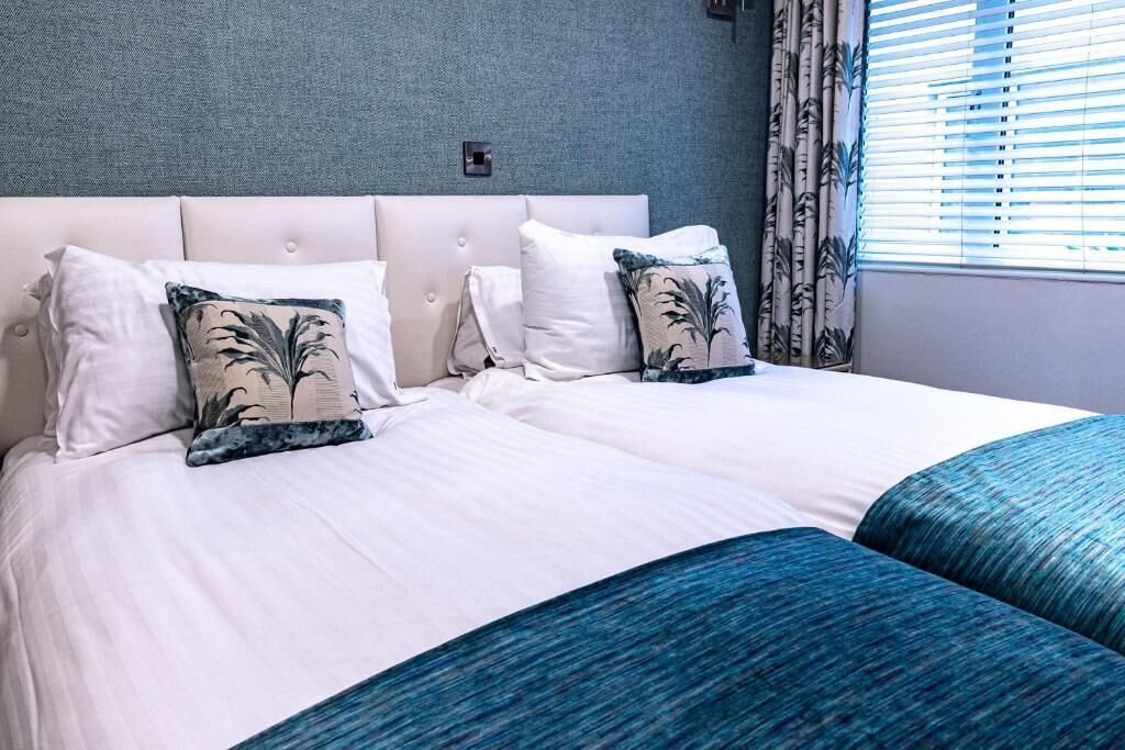 A double bed with white bedding and decorative pillows, a tufted headboard, and a window with curtains.