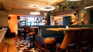 Un ristorante con pavimento a disegno a spina di pesce, un'area bar e posti a sedere con schienali alti e sgabelli.