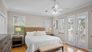 A bedroom with a bed, bedside tables, a bench, a ceiling fan, and large windows with blinds. - 5 Min Walk to Beach | Private Pool | AMI Trolley (Holmes Beach)